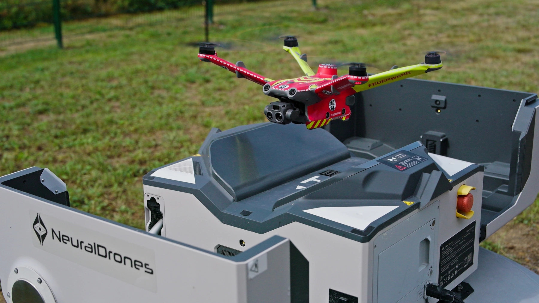 Red and yellow drone above a NeuralDrones-branded docking station outdoors